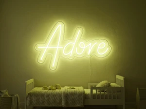 Neonskylt «Adore» i gul LED-neon, monterad på vägg