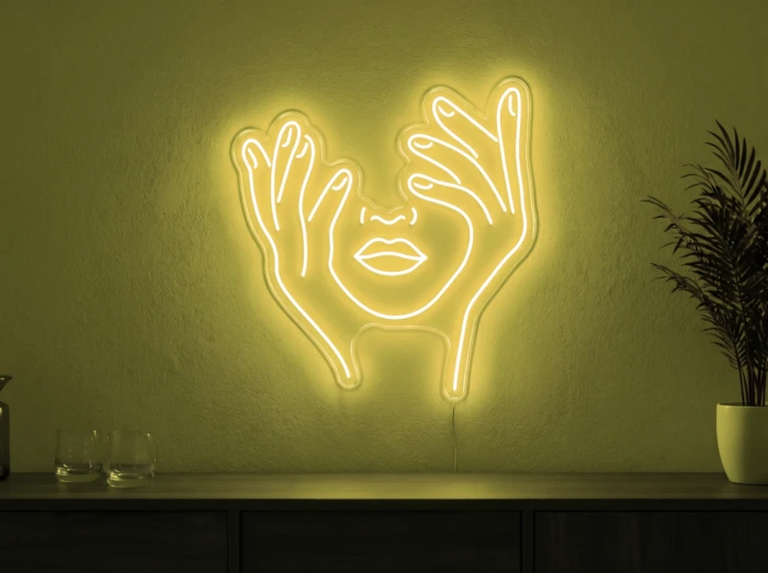 Neonskylt «Ansikte med händer» i gul LED-neon, monterad på vägg