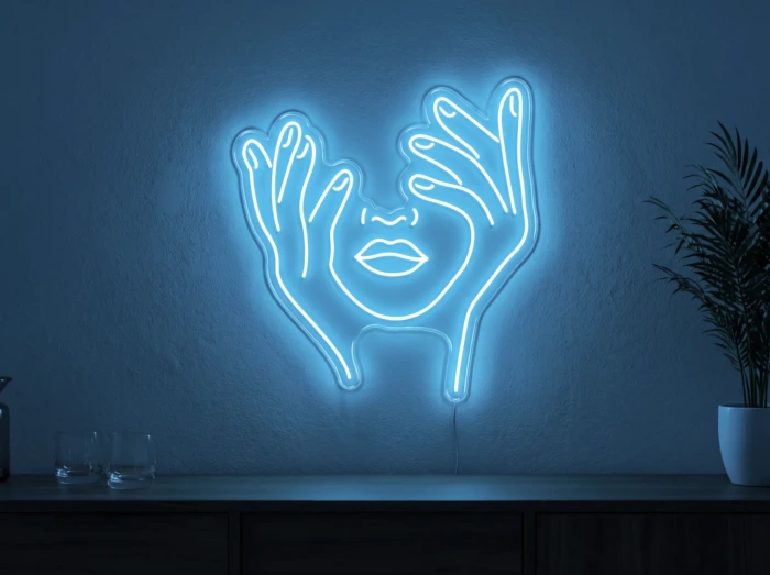Neonskylt «Ansikte med händer» i isblå LED-neon, monterad på vägg