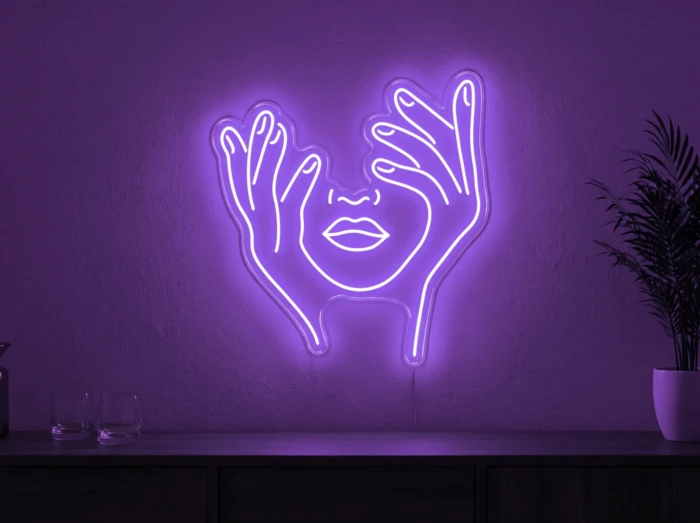 Neonskylt «Ansikte med händer» i lila LED-neon, monterad på vägg