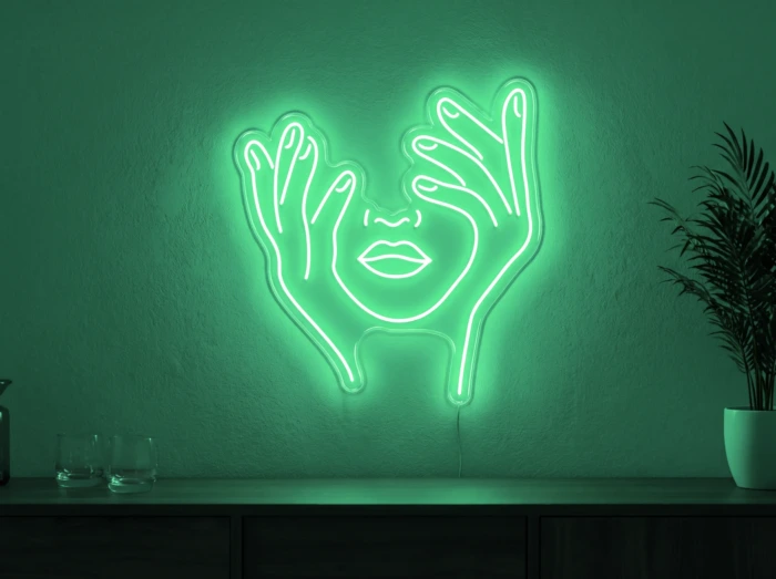 Neonskylt «Ansikte med händer» i mintgrön LED-neon, monterad på vägg