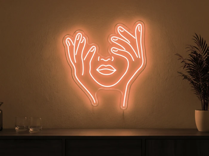 Neonskylt «Ansikte med händer» i orange LED-neon, monterad på vägg