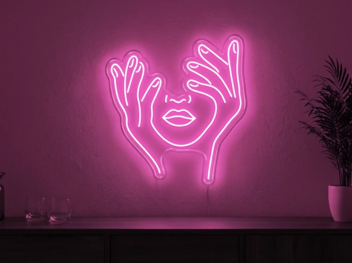 Neonskylt «Ansikte med händer» i rosa LED-neon, monterad på vägg