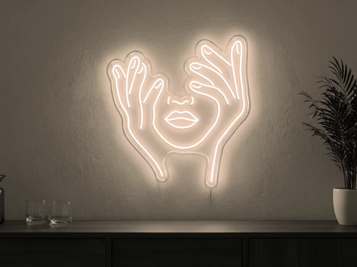 Neonskylt «Ansikte med händer» i varmvit LED-neon, monterad på vägg