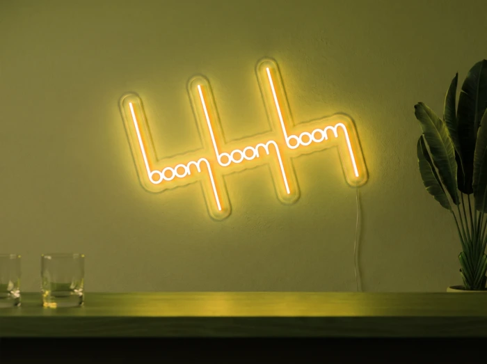 Neonskylt «Boom Boom Boom» i gul LED-neon, monterad på vägg