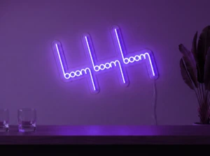 Neonskylt «Boom Boom Boom» i lila LED-neon, monterad på vägg