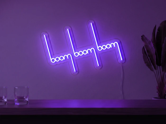 Neonskylt «Boom Boom Boom» i lila LED-neon, monterad på vägg