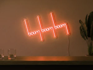 Neonskylt «Boom Boom Boom» i orange LED-neon, monterad på vägg