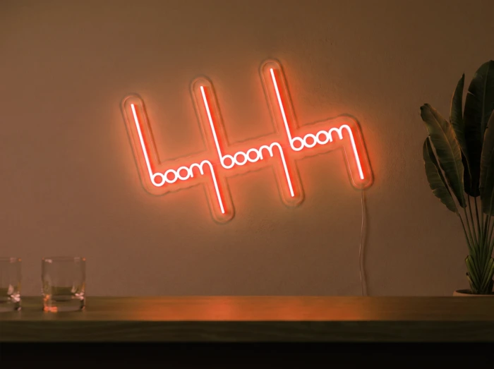 Neonskylt «Boom Boom Boom» i orange LED-neon, monterad på vägg