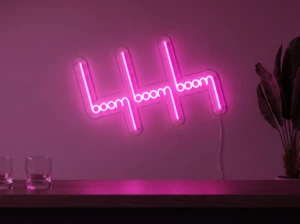 Neonskylt «Boom Boom Boom» i rosa LED-neon, monterad på vägg