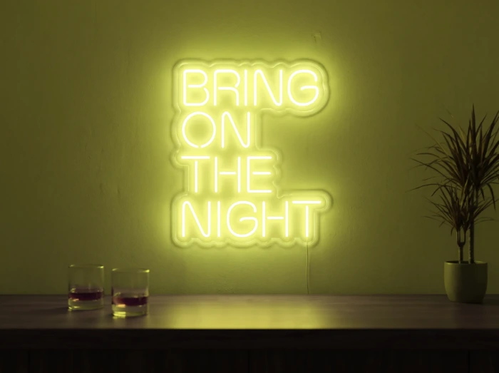Neonskylt «Bring On The Night» i gul LED-neon, monterad på vägg