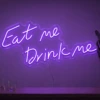 Neonskylt «Eat Me Drink Me» i lila LED-neon, monterad på vägg
