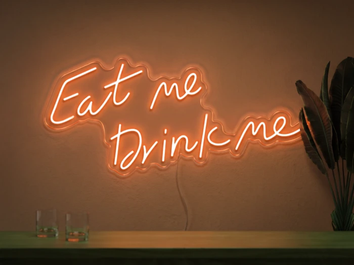Neonskylt «Eat Me Drink Me» i orange LED-neon, monterad på vägg