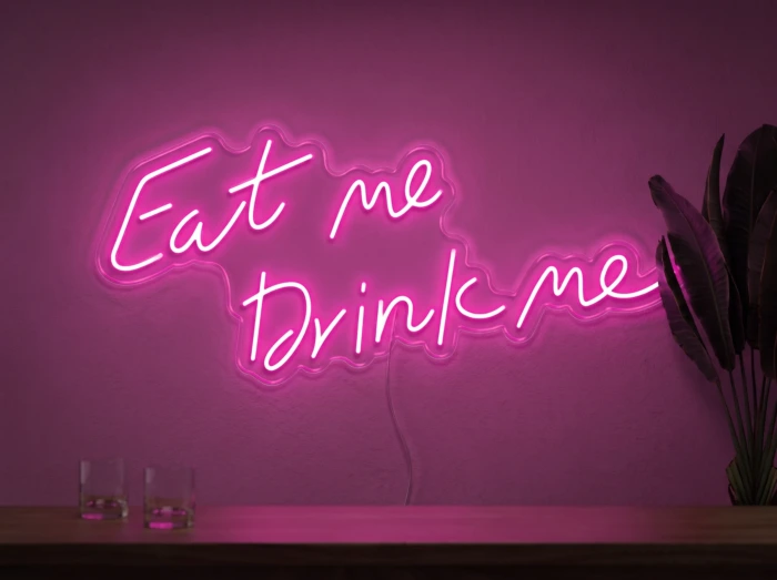 Neonskylt «Eat Me Drink Me» i rosa LED-neon, monterad på vägg