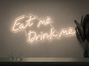 Neonskylt «Eat Me Drink Me» i varmvit LED-neon, monterad på vägg