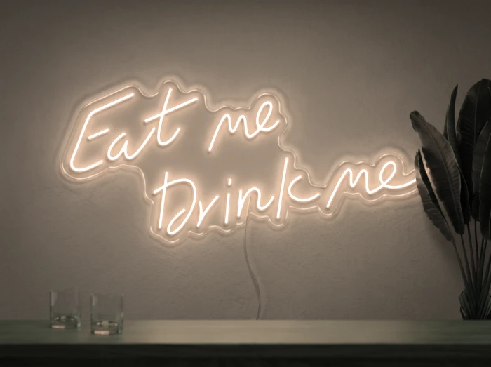 Neonskylt «Eat Me Drink Me» i varmvit LED-neon, monterad på vägg