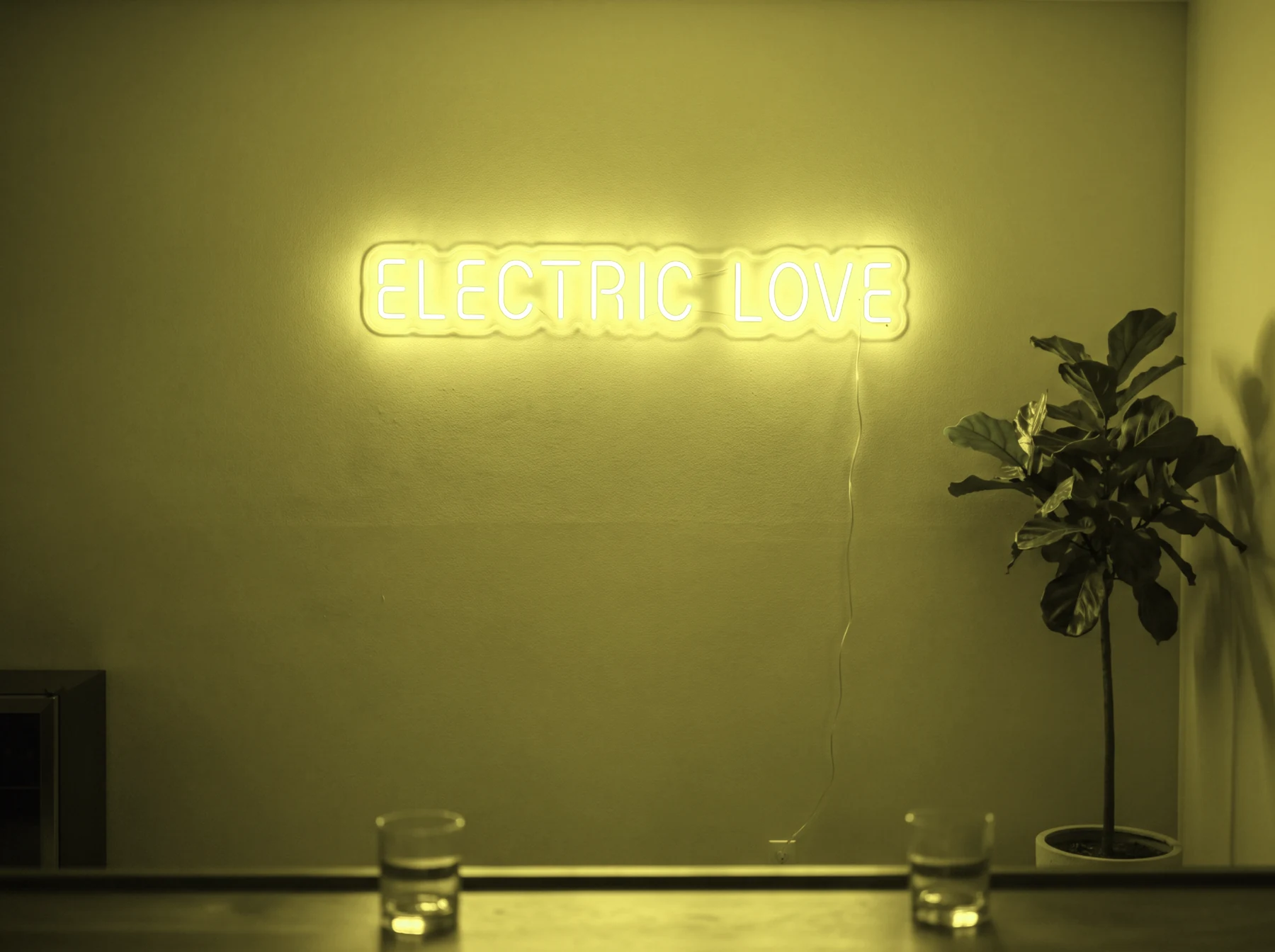 Neonskylt «Electric Love» i gul LED-neon, monterad på vägg