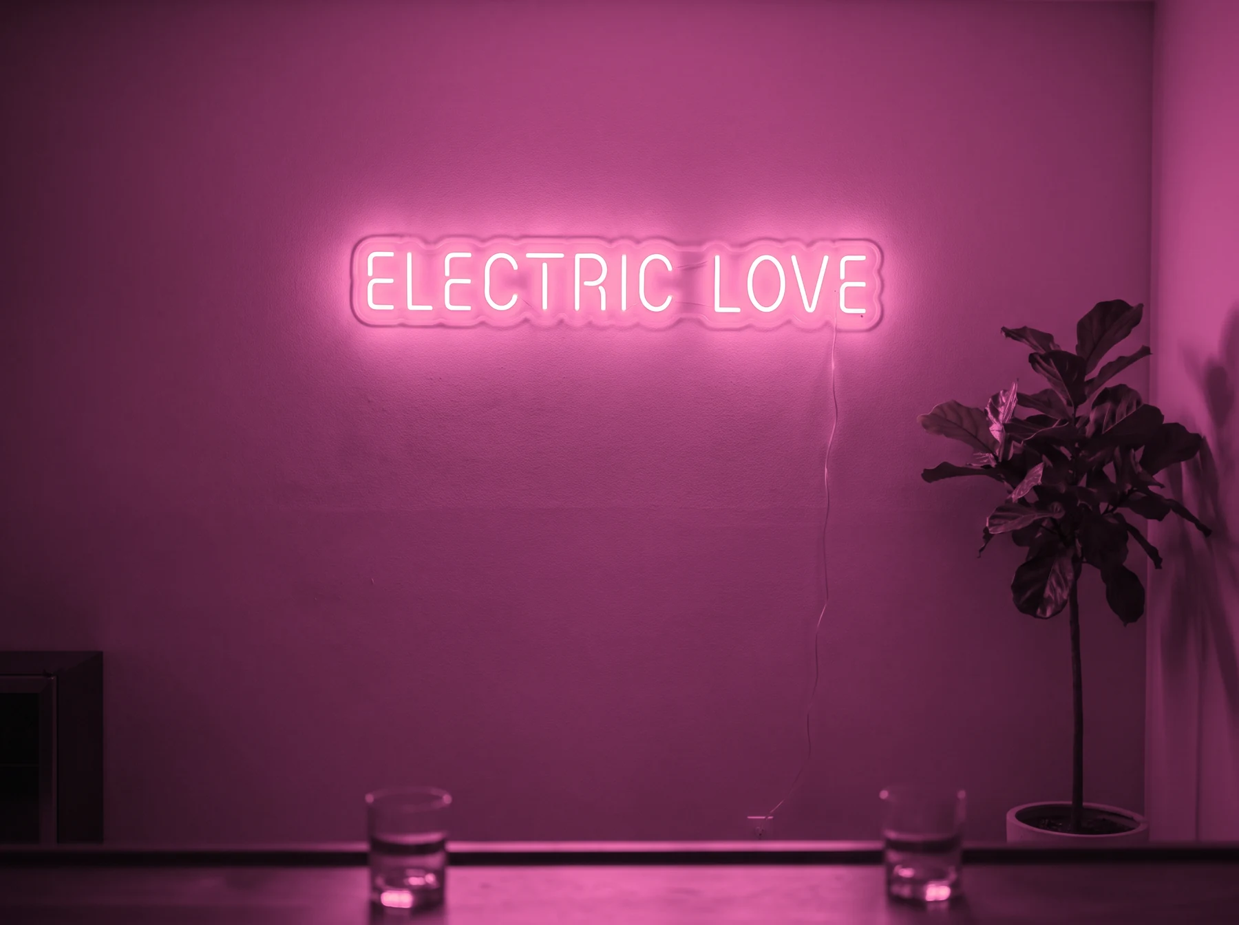 Neonskylt «Electric Love» i rosa LED-neon, monterad på vägg
