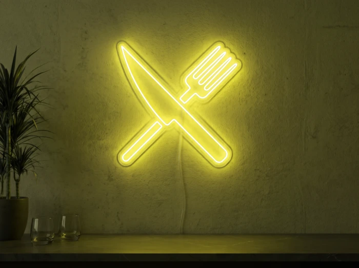 Neonskylt «Gaffel och kniv» i gul LED-neon, monterad på vägg