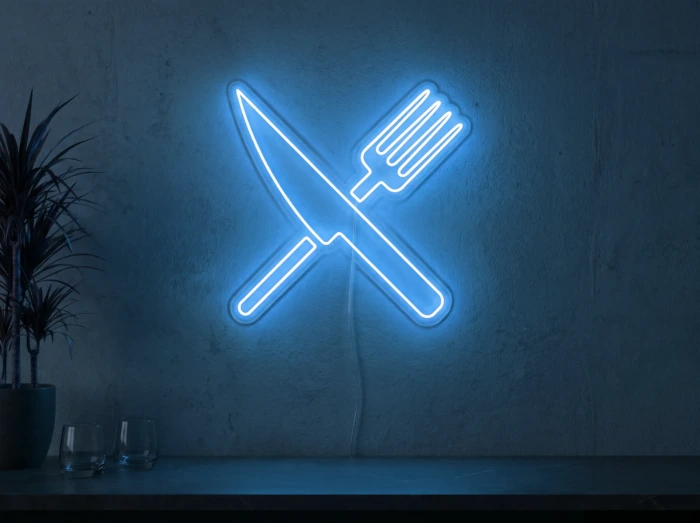 Neonskylt «Gaffel och kniv» i isblå LED-neon, monterad på vägg