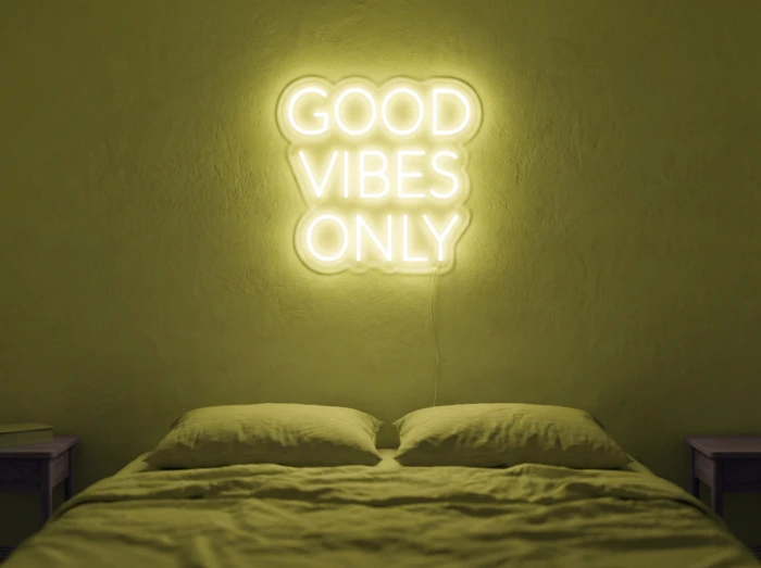 Neonskylt «Good Vibes Only, versaler» i gul LED-neon, monterad på vägg
