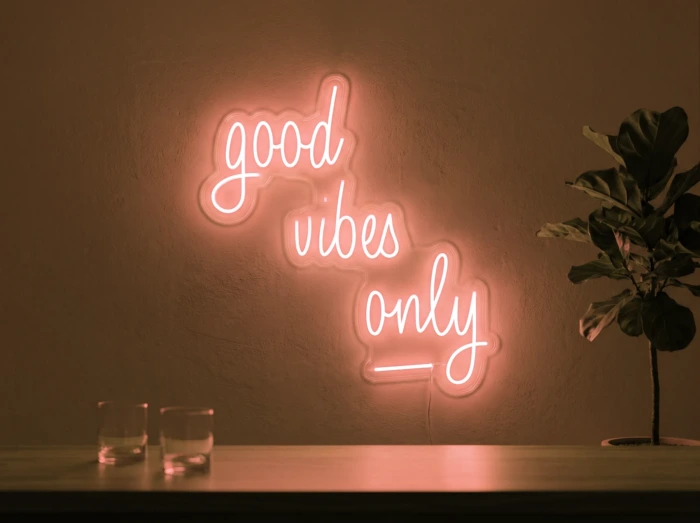 Neonskylt «Good Vibes Only, skrivstil» i orange LED-neon, monterad på vägg