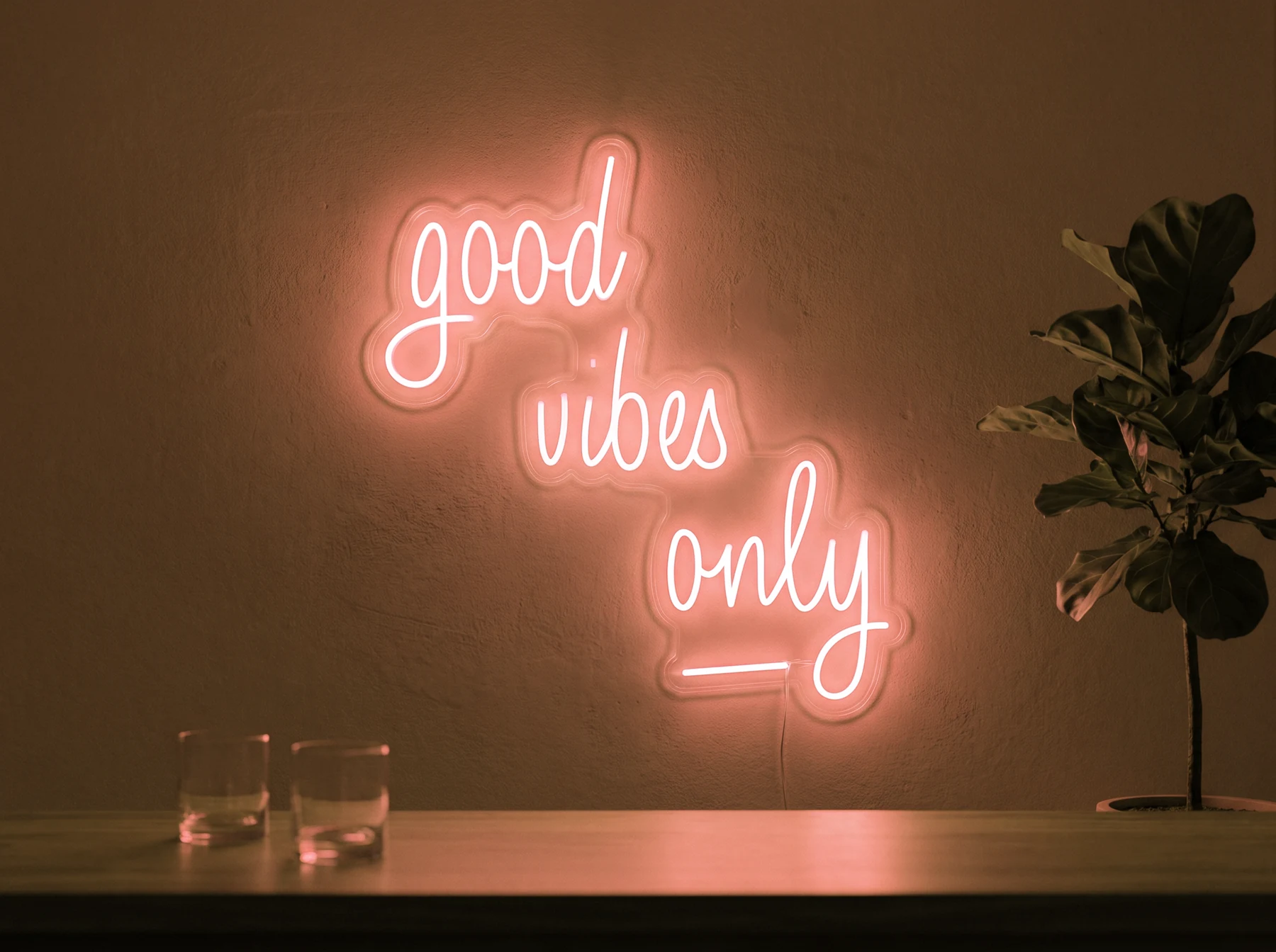 Neonskylt «Good Vibes Only, skrivstil» i orange LED-neon, monterad på vägg