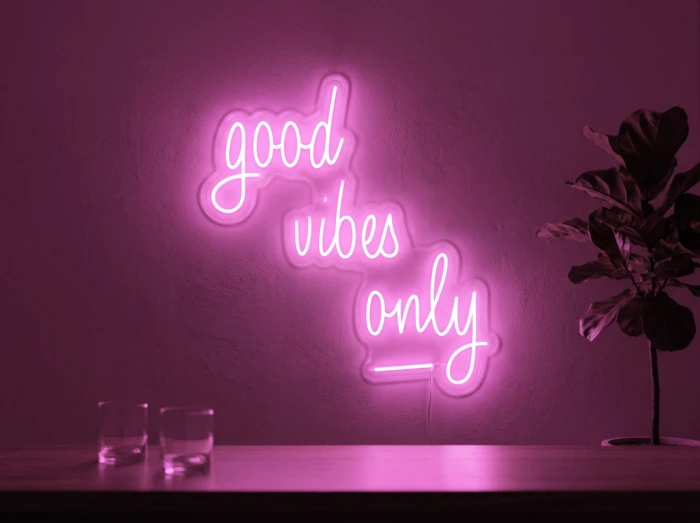 Neonskylt «Good Vibes Only, skrivstil» i rosa LED-neon, monterad på vägg