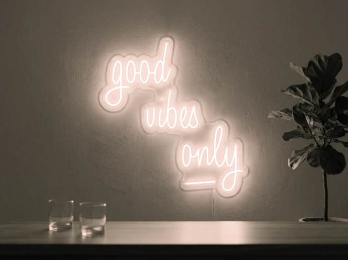 Neonskylt «Good Vibes Only, skrivstil» i varmvit LED-neon, monterad på vägg