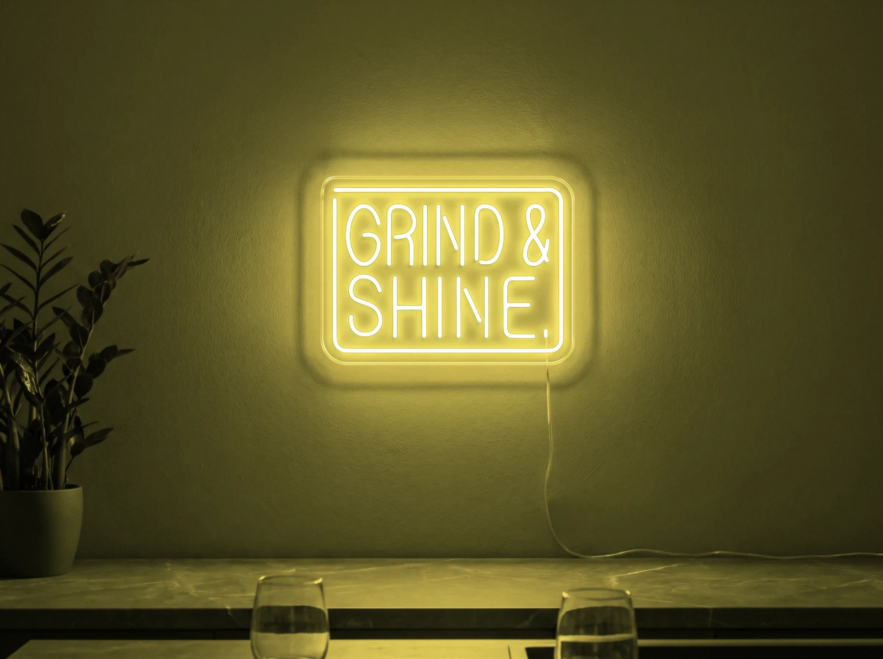 Neonskylt «Grind & Shine» i gul LED-neon, monterad på vägg