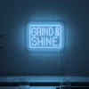 Neonskylt «Grind & Shine» i isblå LED-neon, monterad på vägg