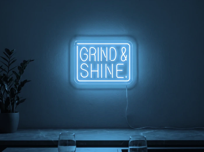 Neonskylt «Grind & Shine» i isblå LED-neon, monterad på vägg