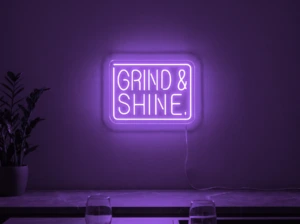 Neonskylt «Grind & Shine» i lila LED-neon, monterad på vägg