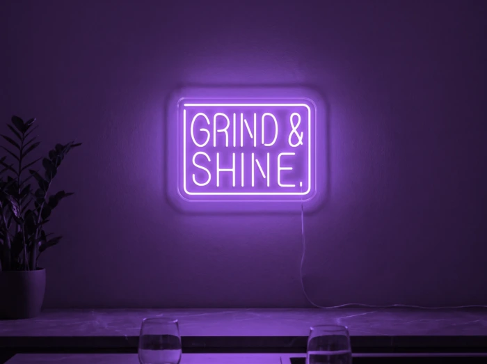 Neonskylt «Grind & Shine» i lila LED-neon, monterad på vägg