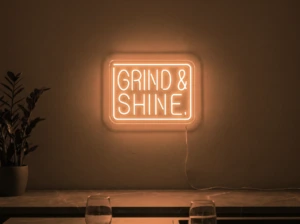Neonskylt «Grind & Shine» i orange LED-neon, monterad på vägg