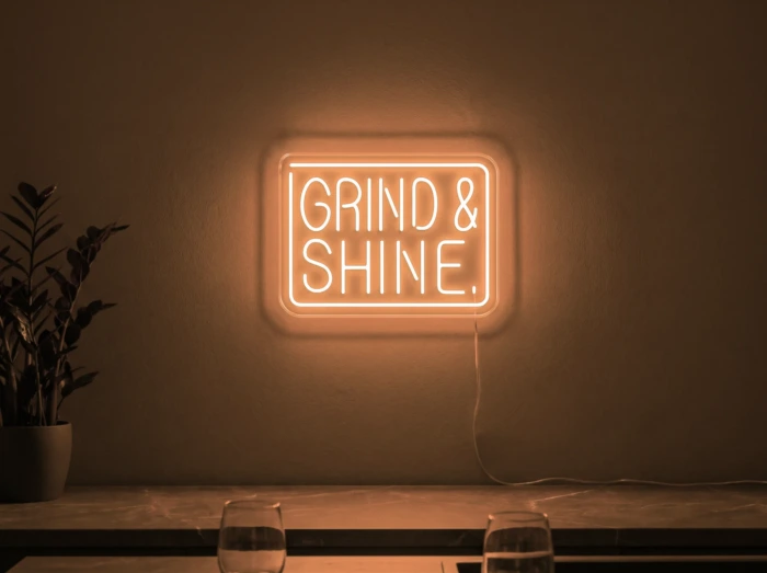 Neonskylt «Grind & Shine» i orange LED-neon, monterad på vägg