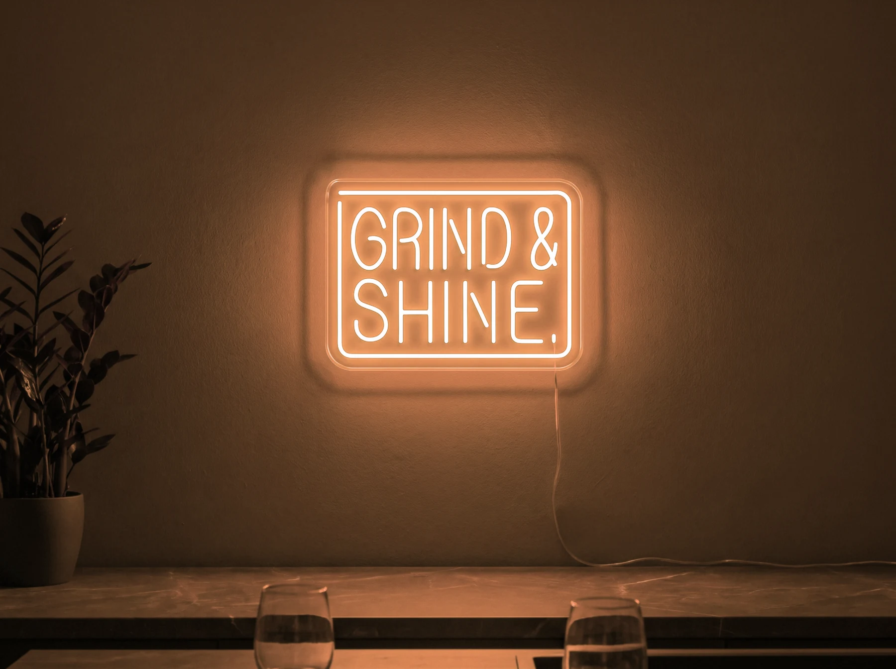 Neonskylt «Grind & Shine» i orange LED-neon, monterad på vägg