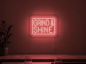 Neonskylt «Grind & Shine» i röd LED-neon, monterad på vägg