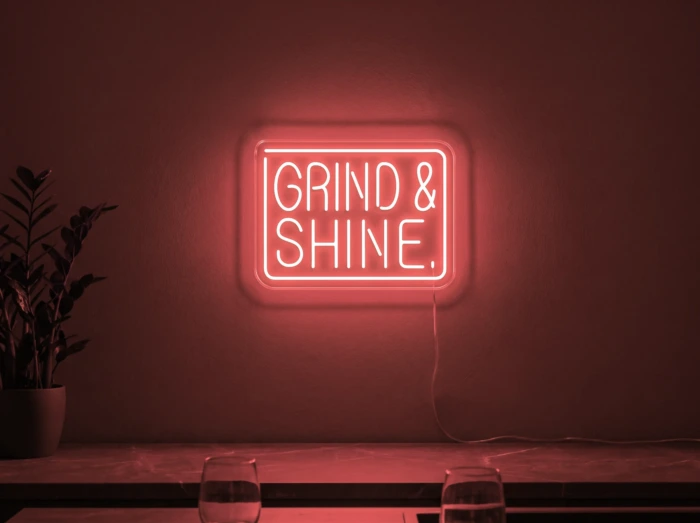 Neonskylt «Grind & Shine» i röd LED-neon, monterad på vägg