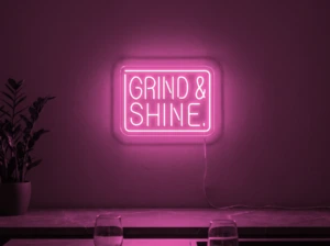 Neonskylt «Grind & Shine» i rosa LED-neon, monterad på vägg