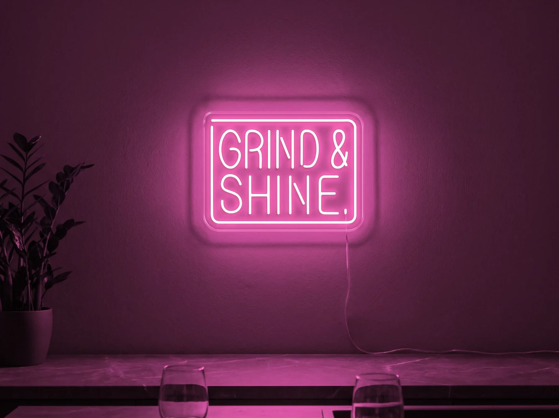 Neonskylt «Grind & Shine» i rosa LED-neon, monterad på vägg