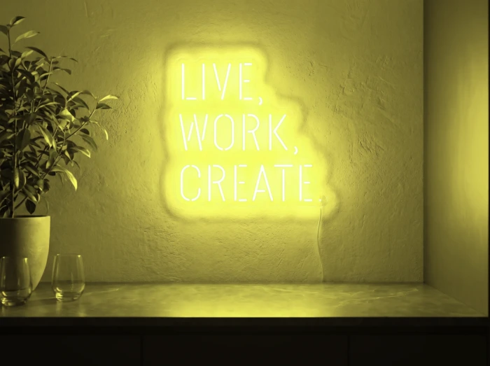 Neonskylt «Live Work Create» i gul LED-neon, monterad på vägg
