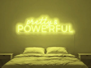 Neonskylt «Pretty And Powerful» i gul LED-neon, monterad på vägg