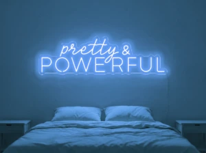 Neonskylt «Pretty And Powerful» i isblå LED-neon, monterad på vägg