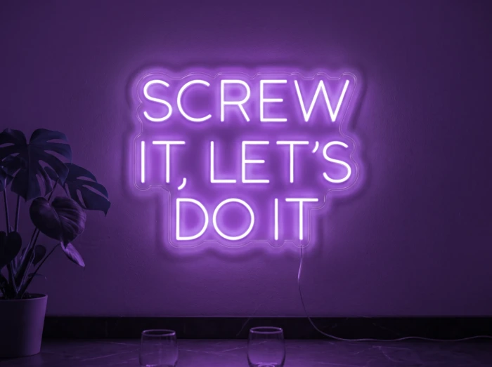 Neonskylt «Screw It Let’s Do It» i lila LED-neon, monterad på vägg