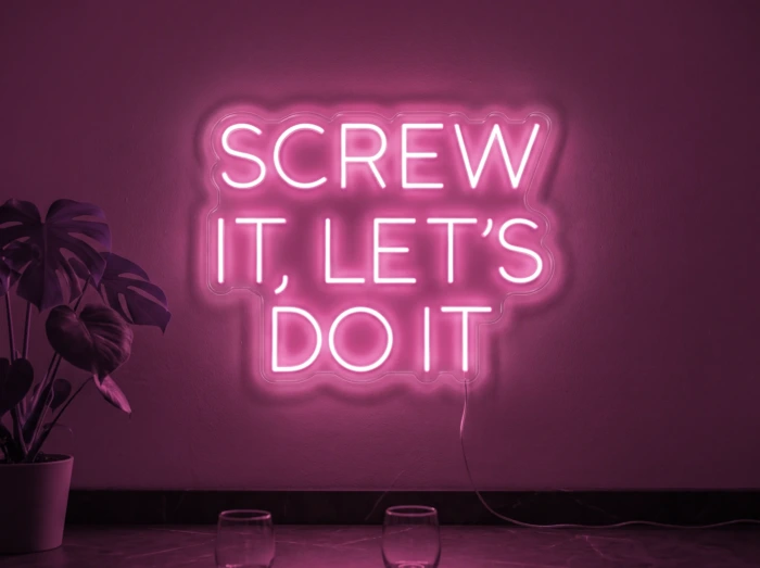 Neonskylt «Screw It Let’s Do It» i rosa LED-neon, monterad på vägg