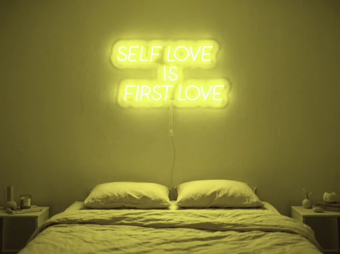 Neonskylt «Self Love Is First Love» i gul LED-neon, monterad på vägg