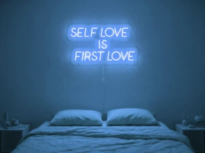 Neonskylt «Self Love Is First Love» i isblå LED-neon, monterad på vägg
