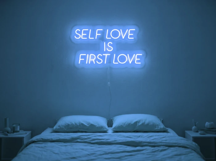 Neonskylt «Self Love Is First Love» i isblå LED-neon, monterad på vägg