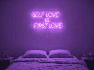 Neonskylt «Self Love Is First Love» i lila LED-neon, monterad på vägg